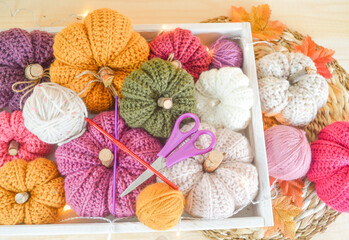 colorful woolen crochet pumpkins with woolen balls, autumn leaves and lights on a wooden tray