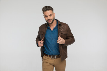 attractive young guy pulling and adjusting brown leather jacket