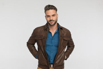 sexy unshaved man holding hands in brown leather jacket's pockets