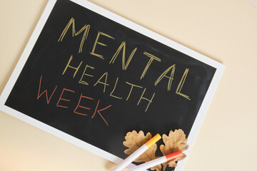 text mental health week on black chalkboard and autumn oak leaves, helping people with mental problems