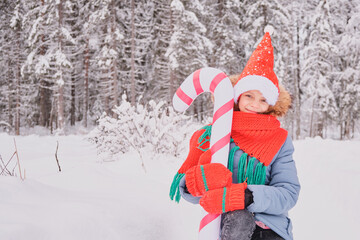 teenage girl in warm snake clothes in christmas flowers outdoor, child in santa hat plays with big inflatable candy cane