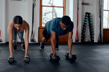 Fototapeta na wymiar Young biracial woman and black man doing plank exercises with weights at the gym