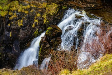 Beautiful waterfall flowing down the rocks covered in moss surrounded by leafless trees