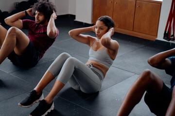 Three determined multiracial young adults doing sit-ups at the gym - obrazy, fototapety, plakaty