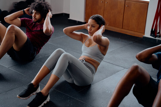 Three determined multiracial young adults doing sit-ups at the gym