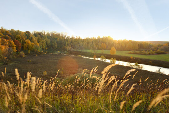 Autumn landscape on the river in a field at sunset with warm sunny office light from a hill from a height