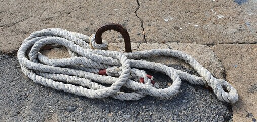 Old white rope on the pier. Marine rope. The old rope lies on the pavement. Tied rope.