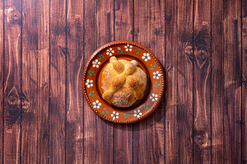 Traditional Mexican bread of the dead also known as "Pan de Muerto" on traditional Mexican tableware on brown wooden background.