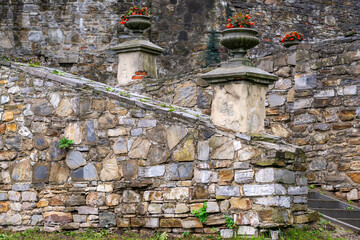 Classical-style stone vases with red flowers on the old stonewall of the park palace