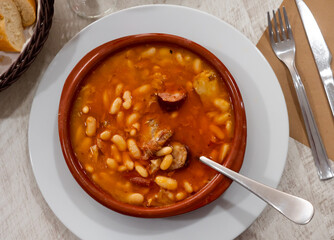 Fabada asturiana served in brown plate with serving pieces