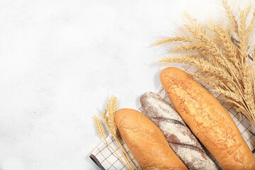 Freshly baked homemade bread, french sourdough baguette with crispy crust and ears of rye and wheat on old concrete background with space for text, modern bakery concept, healthy natural food, 