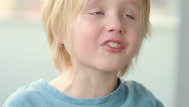 Close-up portrait of crying school-age child. Cute boy with blond hair gets angry and swears. Real emotions. Upset, offended and sad child during a tantrum.
