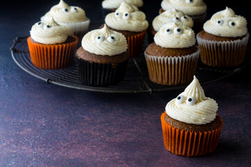 Pumpkin spice cupcakes with ghost shape icing tops, against a dark background.