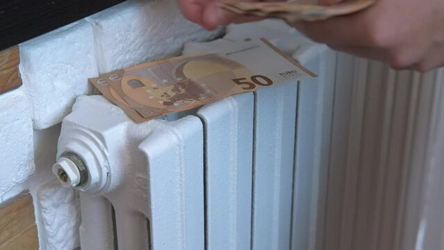 Expensive bills for central heating. A woman puts her money for household and heating on the radiator in the room. A concept of expensive cost of heating during winter crisis time.
