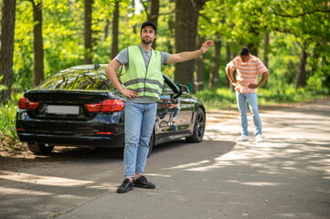 Auto mechanic in a green vest hitchhiking on the forest road