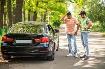 A driver discussing a car accident with a service man and looking uncertain