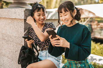 Young gils sitting in the park and spending time in social media