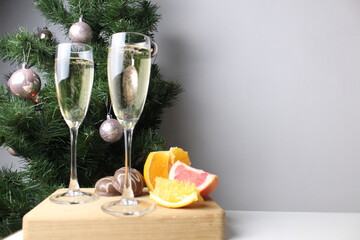 New Year's still life two glasses of champagne and fruit stand against background decorated Christmas tree against gray background with place to insert copyspace text. Celebrating New Year atmosphere