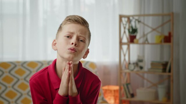 Junior schoolboy begs with palms together in prayer gesture