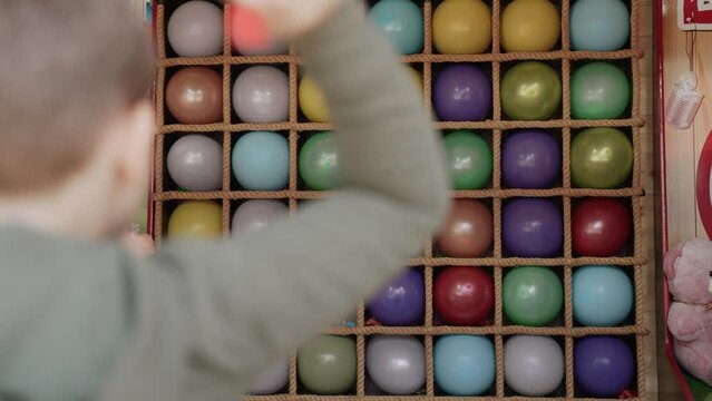 Boy takes aim and throws darts at colorful balloons in amusement park.