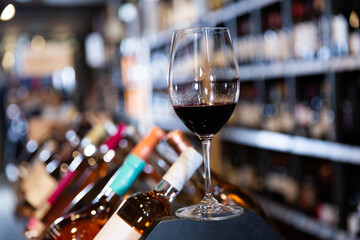 Closeup of red wine glass on blurred background with shelves in wine shop..