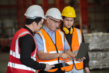 Three man industrial engineers wear hard hats and uniform using laptop talking project of factory inside heavy industry manufacturing. Supervisor teaching work to employee.