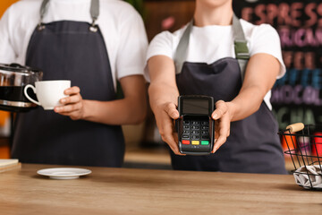 Young baristas with payment terminal in cafe, closeup