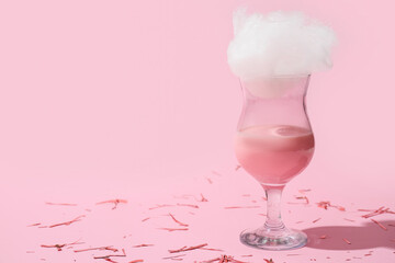 Glass with tasty cotton candy cocktail and confetti on pink background