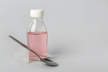 Bottle of cough syrup and spoon on grey background