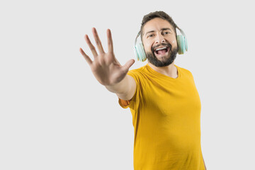 A latin adult man with yellow shirt on white background is listening to music while showing the palm of his hand