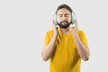 A latin adult man with yellow shirt on white background is listening to music in front of camera