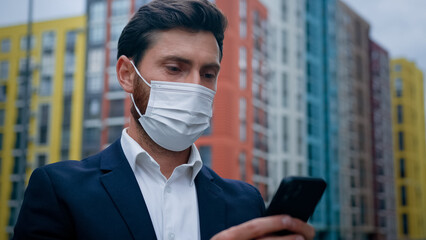 Male businessman in respiratory protection medical mask work on quarantine outdoor texting on smartphone at street professional chat with colleagues online using mobile business apps free wifi outside