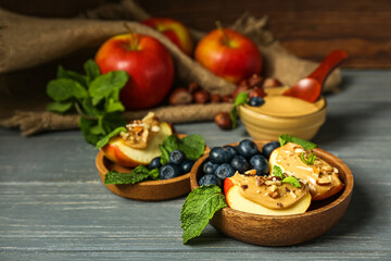 Bowls of tasty apple wedges with nut butter, blueberry and mint on dark wooden table