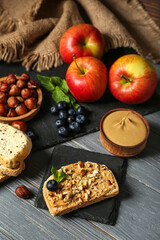 Tasty sandwich with nut butter, apples, hazelnuts and blueberry on dark wooden background