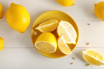 Plate with fresh lemons on light wooden background