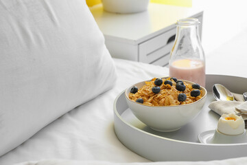 Tray with bowl of cornflakes, boiled egg and yogurt on bed, closeup
