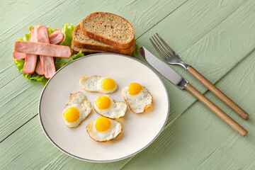 Plate with fried quail eggs, sausages and bread on color wooden background