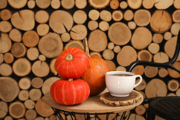 Table with fresh pumpkins and cup of coffee near wooden wall, closeup