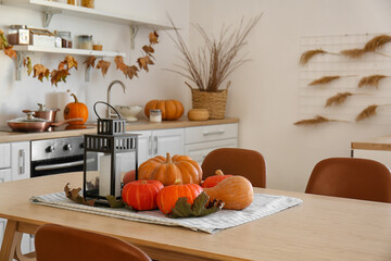 Halloween pumpkins with lantern and leaves on dining table in kitchen