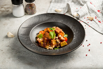 fried eggplant in sweet sour sauce with tomatoes and cilantro on dark plate on grey table