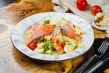Caesar salad with salmon on wooden table
