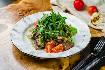 Steak salad with beef, aragula, vegetables, mushrooms and sesame on wooden table