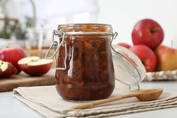 Delicious apple jam in jar and wooden spoon on table
