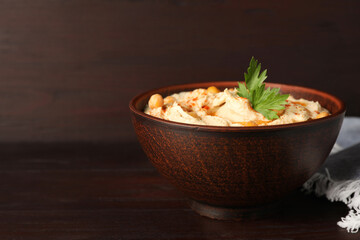 Bowl of tasty hummus with chickpeas and parsley on wooden table, space for text