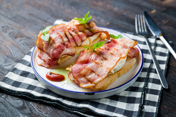 eggs Benedict with bacon on dark wooden table side view