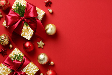 Luxury Christmas gifts and ornaments on red background. Elegant Christmas background with presents, golden and red baubles top view.