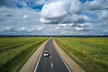 Aerial view of intercity road between green agricultural fields with fast driving car. Top view from drone of highway traffic