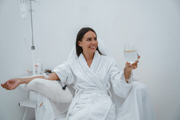 Beautiful woman in white bathrobe drink water during medical procedure in beauty clinic