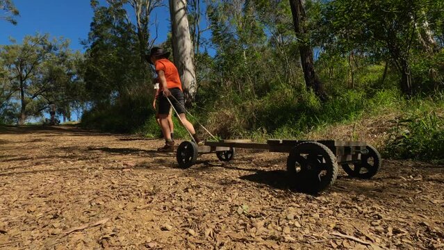 Farm boys pull a wooden go-cart up a steep dirt country road in Australia
