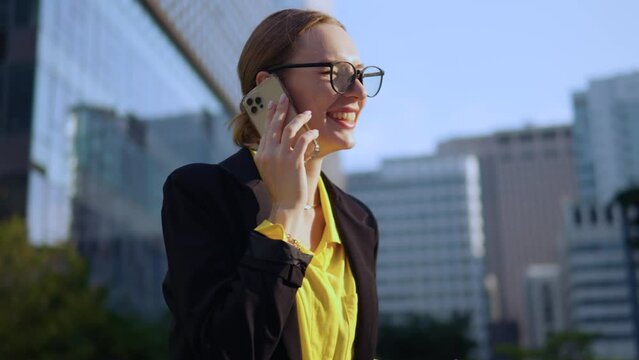 Funny business woman laughing out loud while talking on phone outside office buildings and trying to cool down